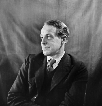 Ein Mann im Anzug sitzt vor einem strukturierten Hintergrund.