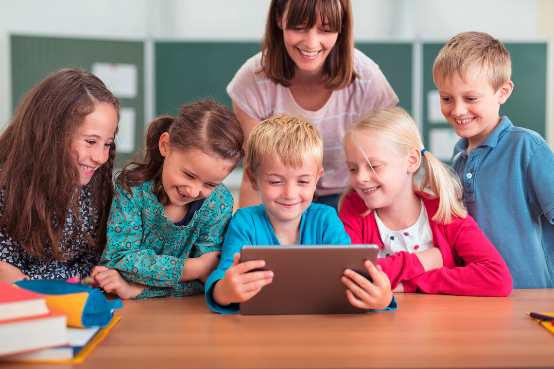 Lehrerin mit 5 Grundschüler*innen vor einem Tablet