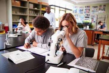 Schüler und Schülerin gucken im Biologieunterricht durch ein Mikrosop