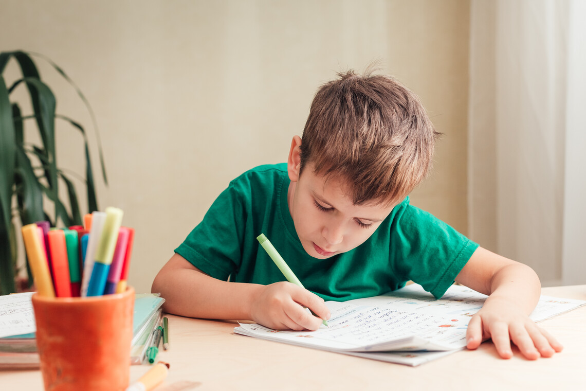 Junge im grünen T-Shirt sitzt an seinem Schreibtisch und lernt schreiben