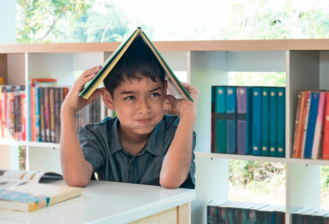 Junger Schüler mit aufgeschlagenem Buch über dem Kopf