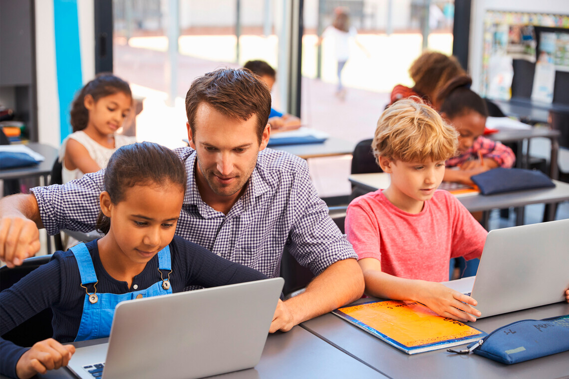 Lehrer hilft Schüler*innen mit dem Laptop zu arbeiten