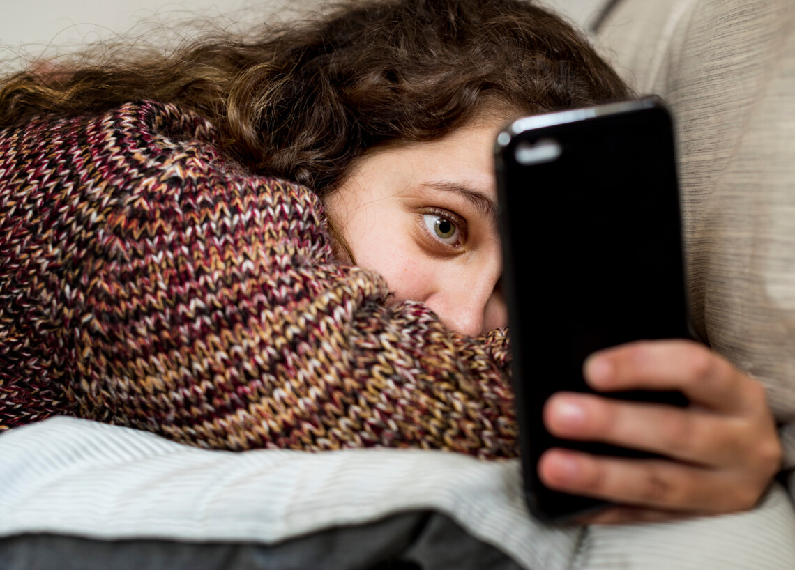 Mädchen liegt mit Smartphone auf dem Sofa