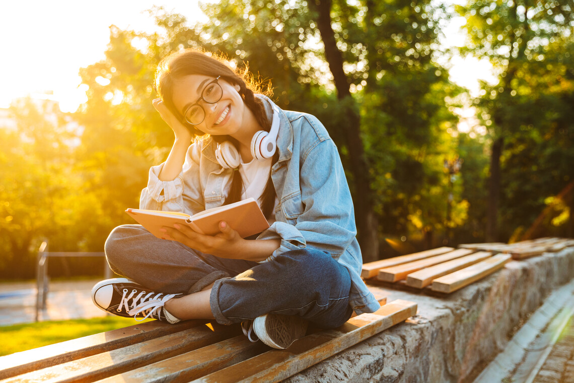 Junge Frau liest draußen beim Sonnenuntergang
