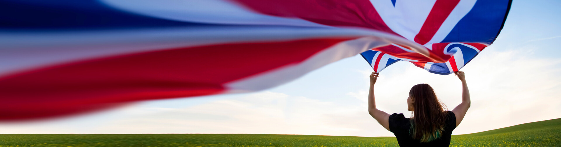 Person hält britische Flagge; Hintergrund: blühendes Feld und Himmel bei Sonnenuntergang.