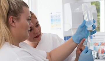 Zwei Personen bereiten einen Infusionsbeutel vor, tragen weiße Kittel und blaue Handschuhe.