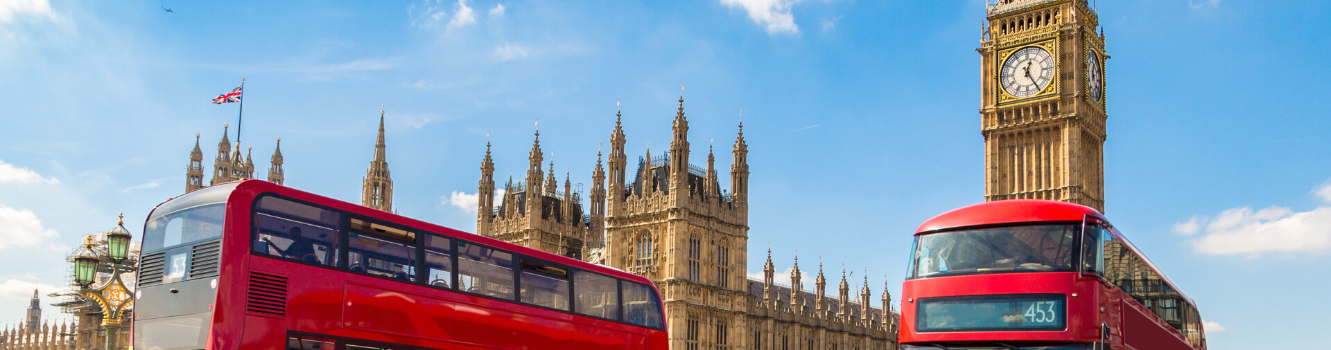 Zwei rote Londoner Busse fahren vor dem Big Ben und den Houses of Parliament vorbei.