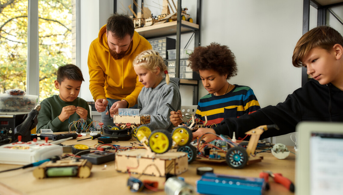 4 Schüler/-innen und ein Lehrer experimentieren mit Robotern