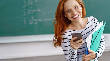 Eine Person mit rotem Haar hält Smartphone und Ordner vor einer grünen Tafel.