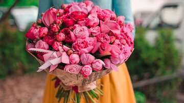 Ein Blumenstrauß mit pinken Rosen und Tulpen in Zeitungspapier eingewickelt.