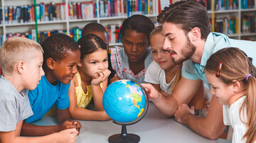 Eine Gruppe von Kindern und ein Mann schauen auf einen Globus. Der Mann zeigt auf den Globus. 