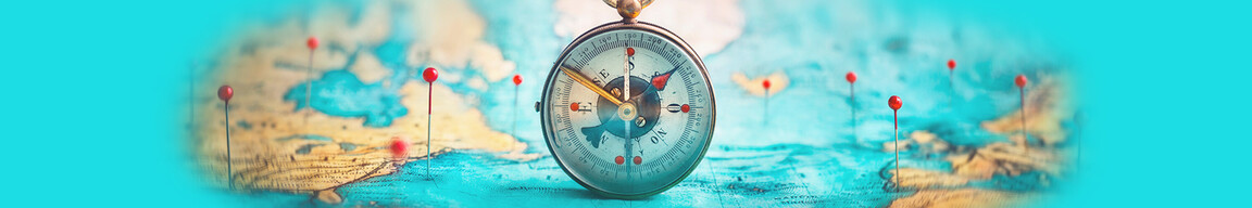 Ein Kompass steht aufrecht auf einem Atlas in dem rote Stecknadeln stecken