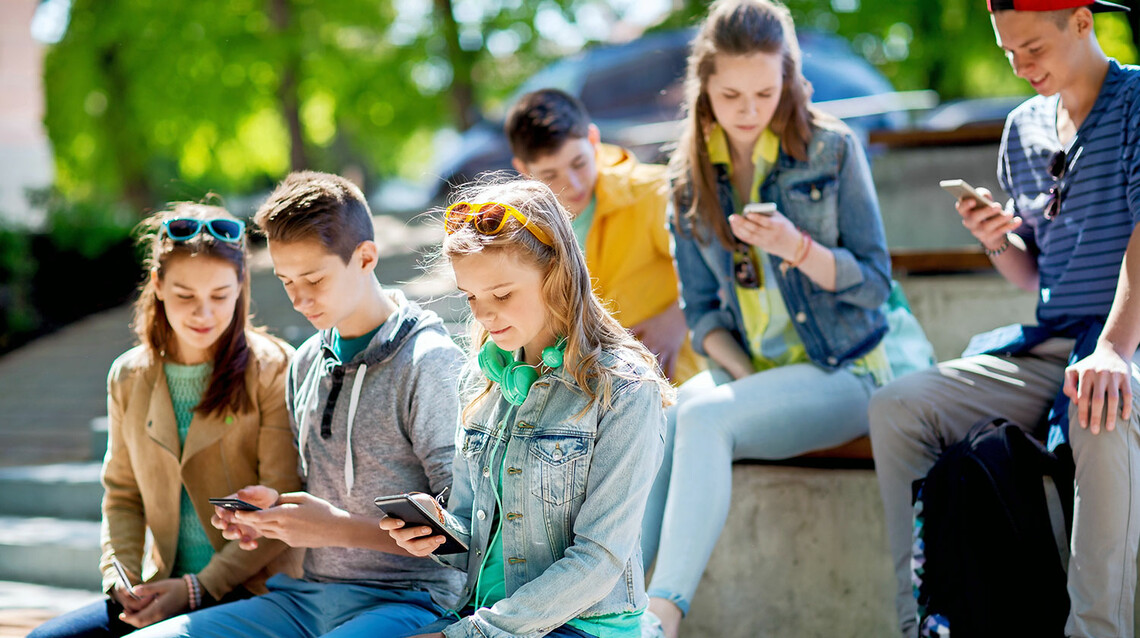 Schüler*innen sitzen draußen mit Smartphones