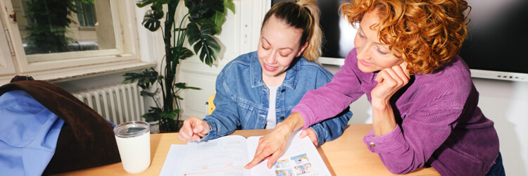 Lehrerin erklärt einer Schülerin eine Aufgabe in einem Schulbauch in einem Klassenraum