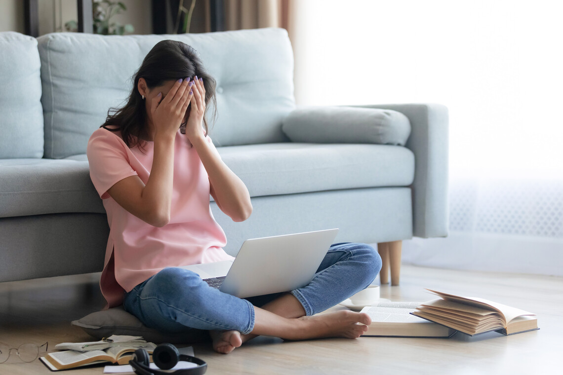 Lehrerin sitzt verzweifelt vor ihrem Sofa mit dem Laptop auf dem Schoß