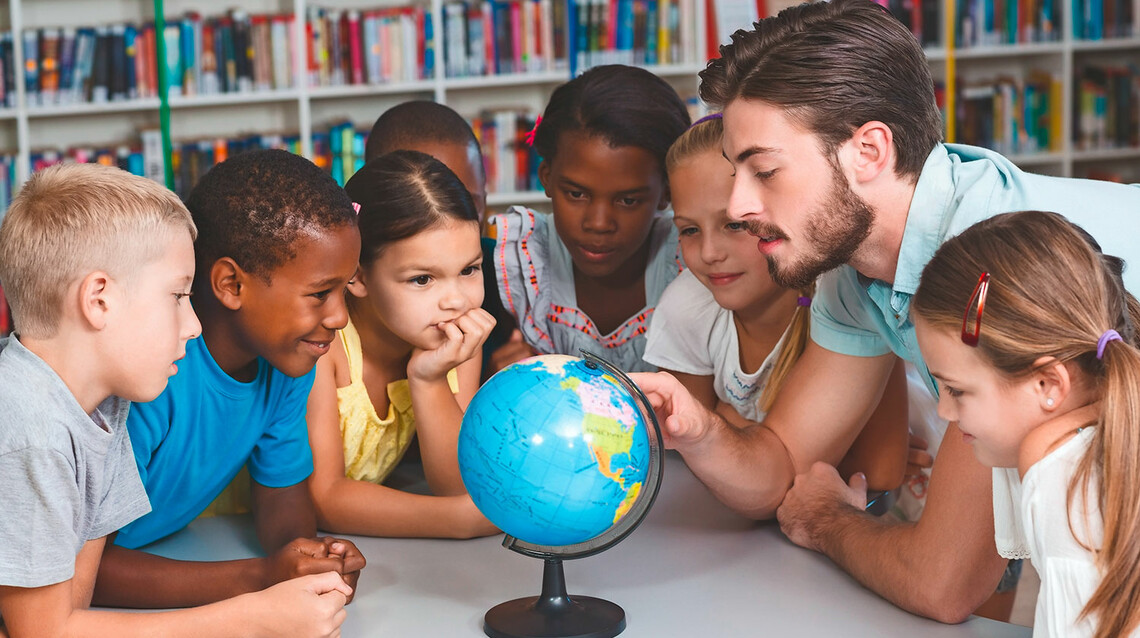 Klassenlehrer mit Grundschulkindern vor einem Globus