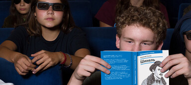 Menschen sitzen in einem dunklen Kinosaal und lesen Programmhefte.