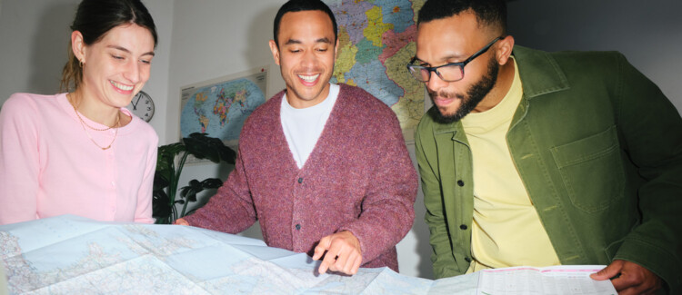 Fünf junge Erwachsene, stehen im Klassenraum und schauen auf eine ausgefaltete Europa-Karte, im Hintergrund ein Smartboard