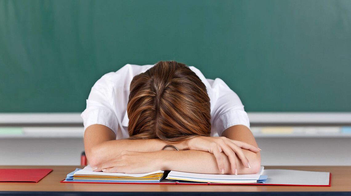 Junge Lehrerin liegt mit dem Kopf auf dem Tisch