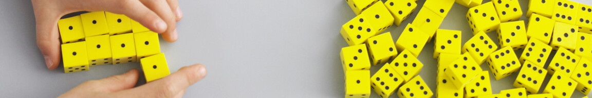 Zwei Hände ordnen gelbe Würfel; viele Würfel liegen rechts. Hellgrauer Hintergrund.