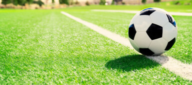 Ein Fußball auf einem grünen Spielfeld mit weißen Linien unter Sonnenschein.