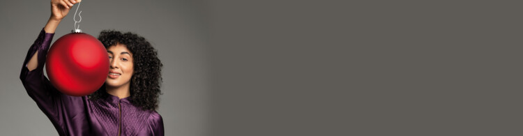 Person hält großen roten Weihnachtsbaumschmuck im Studio, trägt lila Oberteil.