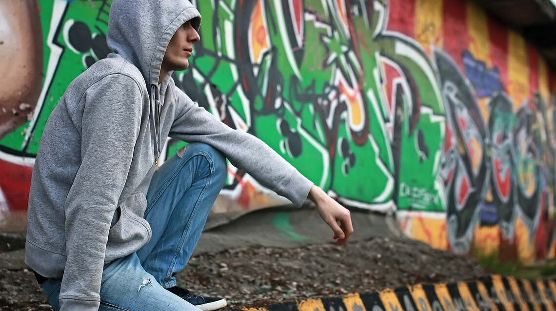 Jugendlicher mit Kapuze vor einem Graffiti