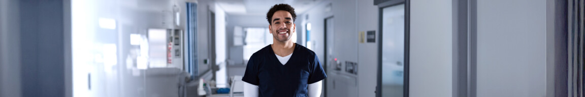 Young adult male healthcare worker standing in hospital corridor, smiling with medical cart behind. Clinician, scrubs, uniform, professional, clinical, sterile, caregiving; Shutterstock ID 2621343449; client: 837; job: picturemaxx; other: susanne.finke@cornelsen.de; purchase_order: picturemaxx
Young adult male healthcare worker standing in hospital corridor, smiling with medical cart behind. Clinician, scrubs, uniform, professional, clinical, sterile, caregiving